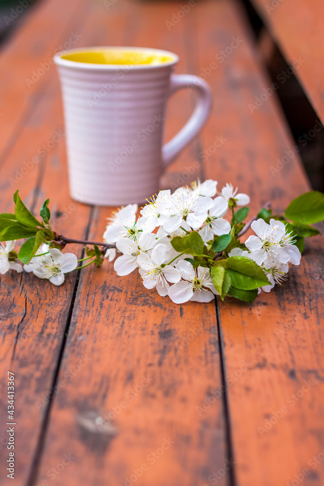 a cup of coffee on a dark, worn rustic wooden table. The composition is decorated with a twig with white flowers. Cherry tree flowers. Selective focus.