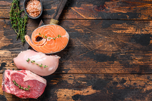 Different types of raw meat steaks Beef striploin, salmon and chicken breast. Dark wooden background. Top view. Copy space photo