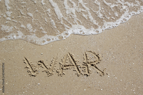 The word "war" on the sea sand, written with a finger with an oncoming sea wave and foam. A symbol stop the war