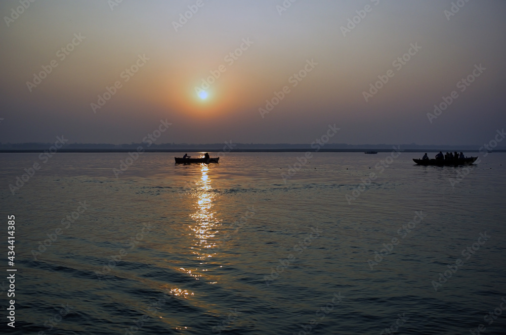 Varanasi, India: Wide angle Silhouette shot of People and tourists on wooden boat sightseeing in ganges river close to famous Munshi ghat during sunrise or sunset. Varanasi, India: Wide angle Silhouette shot of People and tourists on wooden boat sightseeing in ganges river close to famous Munshi ghat during sunrise or sunset.