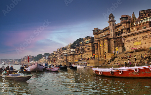 Varanasi, India: People and tourists on wooden boat sightseeing in Ganges river near Munshi ghat against ancient city architecture as viewed from a boat during morning time