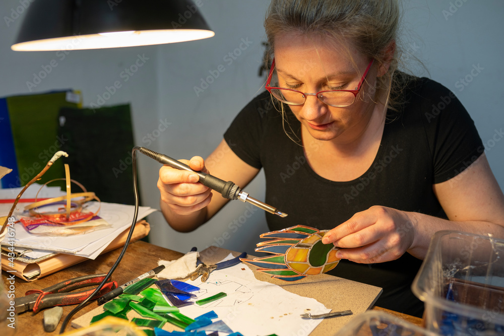 soldering the stained glass window, woman is making a stained glass