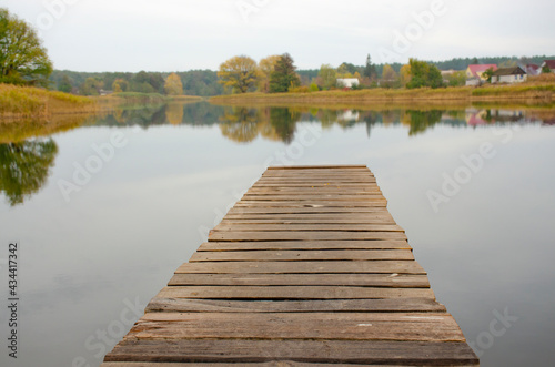 Perspective view of wooden pier at lake. Small bridge in water. Empty wooden bridge or table top with the rural lake and sky landscape. Nature park background and autumn season