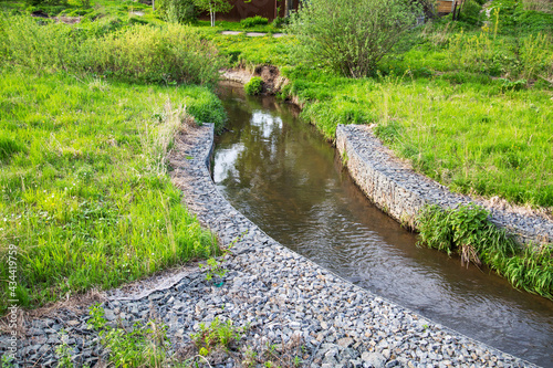 Photos A channel made of granite stones for the river stream with grass and shrubs on the banks