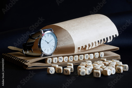 Принти на полотні A wristwatch, a notebook and the word linguistics, made up of wooden cubes, on a dark background
