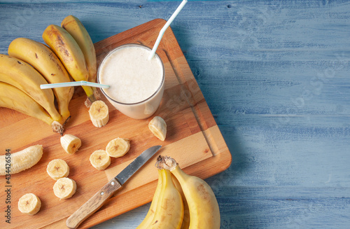 Vista cenital de una tabla de cortar con un vaso de batido de  leche y plátanos con algunas rodajas de plátanos y ademas mas plátanos rodeando el vaso photo