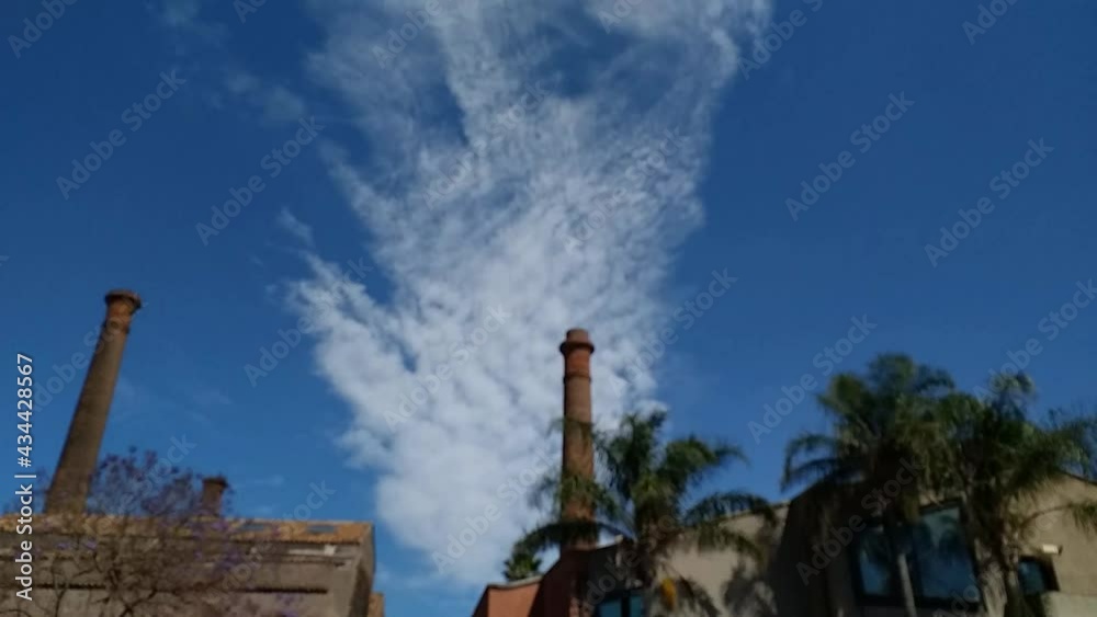 Time lapse di una bellissima nuvola che scorre in verticale allontanandosi dal punto di ripresa video, con edifici e ciminiere in primo piano sfocati