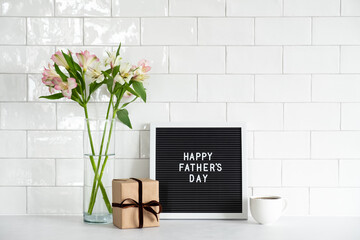 Happy Fathers day concept. Letterboard with text Happy Father's Day, gift box, cup of coffee, buquet of flowers on table. Tile on background.