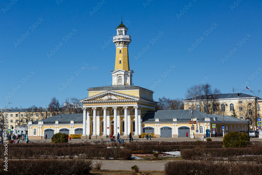Kostroma, Russia. Central Susaninskaya Square. Famous Fire Observation Tower in early spring. Old yellow classical building against blue sky