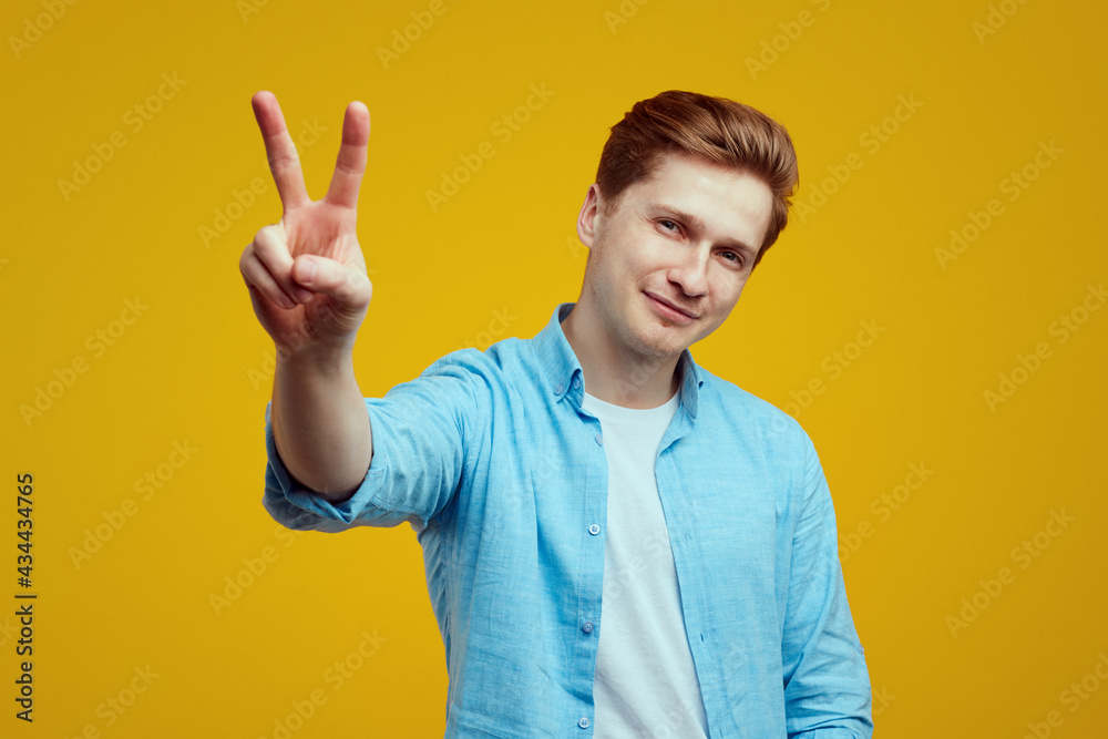 Man in wearing blue shirt and showing peace gesture over yellow backdrop Man in wearing blue shirt and showing peace gesture over yellow backdrop