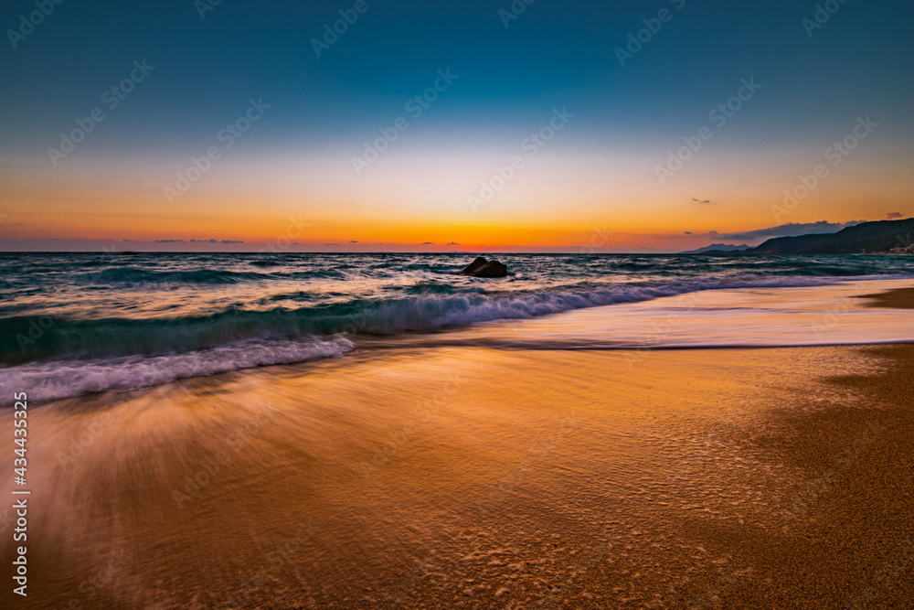 Ocean water flowing over rocks and beach with golden sunrise