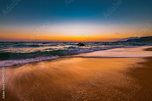 Ocean water flowing over rocks and beach with golden sunrise