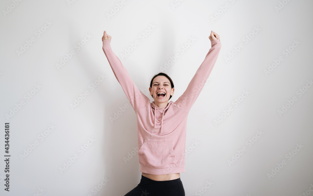 Millennial young woman in pink hoodie on white background. Women empowerment concept. Hands up happy woman. Feminism superwoman portrait Millennial young woman in pink hoodie on white background. Women empowerment concept. Hands up happy woman. Feminism superwoman portrait