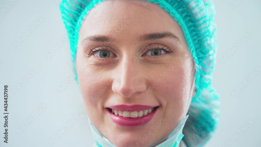 Doctor in medical hat taking off mask and smiling in the dental office looking into the camera Doctor in medical hat taking off mask and smiling in the dental office looking into the camera