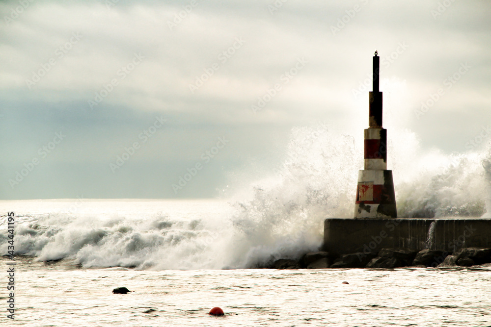 Obraz premium Giant waves breaking on the breakwater and the lighthouse