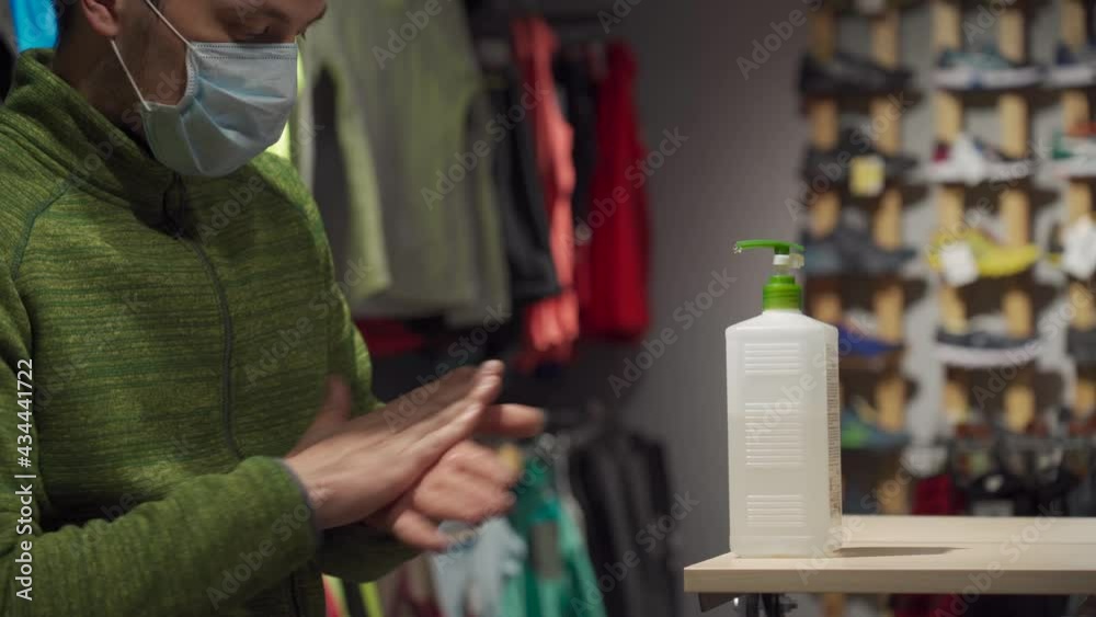 Buyer uses antiseptic gel in sporting goods store during coronavirus quarantine. New norm, no mask no entrance. Disinfecting hands with sanitizer before shopping. Alcohol dispenser for cleaning hand Buyer uses antiseptic gel in sporting goods store during coronavirus quarantine. New norm, no mask no entrance. Disinfecting hands with sanitizer before shopping. Alcohol dispenser for cleaning hand