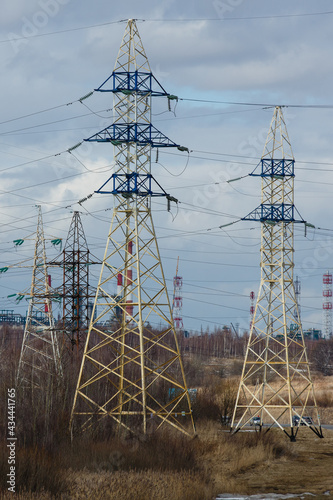 Electricity pylons against the constructions of oil refinery in the early  spring. High voltage power line supports or posts. Transmission towers of electric power lines in Yaroslavl region, Russia