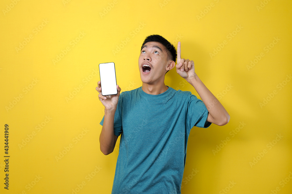 Happy smiling young Asian man showing mobile phone with another hand pointing to empty space Happy smiling young Asian man showing mobile phone with another hand pointing to empty space