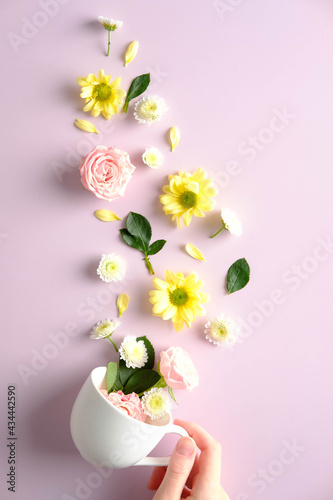 Female hand holding tea cup with flowers on pnik background. Creative flat lay composition, top view. photo