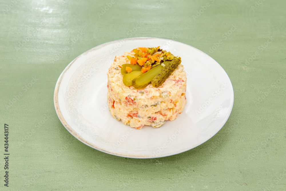 Russian salad top with pickled gherkins on white plate Russian salad top with pickled gherkins on white plate