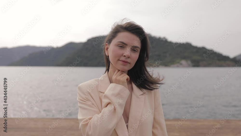 Close up portrait of Beautiful Young Woman in jacket smiling. Hair blowing in wind on tropical beach slow motion Close up portrait of Beautiful Young Woman in jacket smiling. Hair blowing in wind on tropical beach slow motion