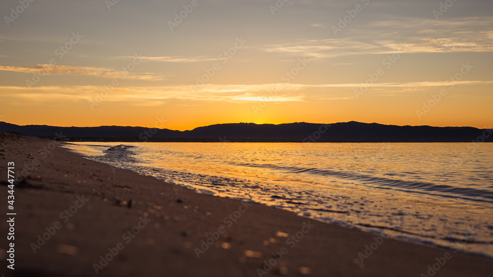 Naklejka premium Long distance view of small waves crushing the shore of Poetto beach at sunrise
