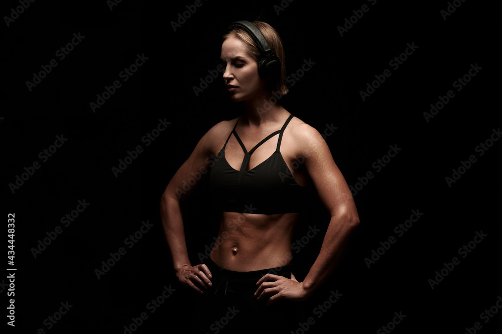 Obraz premium Young female with muscular body getting ready to workout and listen music in headphones