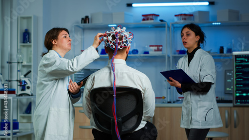 Man patient wearing performant eeg headset scanning brain electrical activity in neurological research laboratory while medical researcher controlling it, examining nervous system, nurse taking notes photo