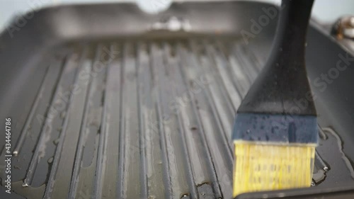 Close-up brushing with a silicone brush a grilling pan with olive oil in 4K. Concept of moisturizing a cooking pan before frying.