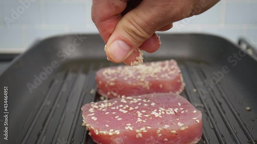 Seasoning with salt pepper and sesame seed yellowfin tuna steak on grilling pan. Concept of grilling a tuna steak and sprinkling spices on top in 4K.
