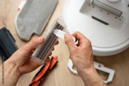 A man cleans the hepa filter from a robot vacuum cleaner with a special brush