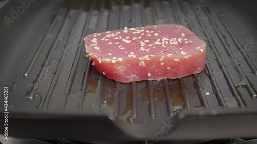 Placing a raw steak of yellowfin tuna into a grilling pan in 4K. Concept frying and cooking tuna steak in slow motion.