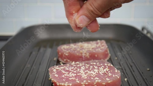 Seasoning with salt pepper and sesame seed yellowfin tuna steak on grilling pan. Concept of grilling a tuna steak and sprinkling spices on top in 4K.
