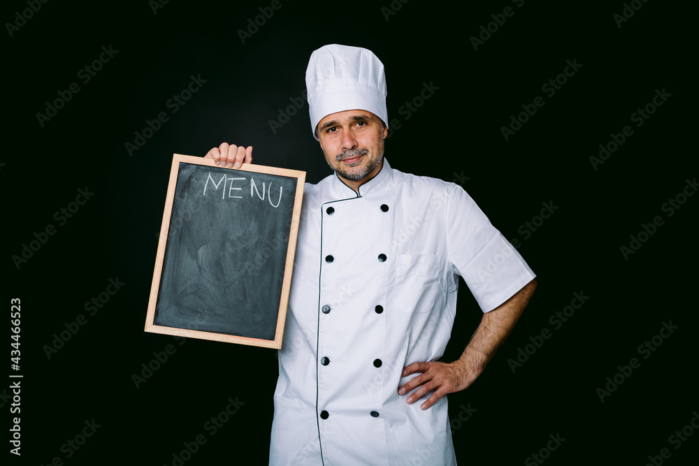 Chef cook in jacket and kitchen hat smiling, holding a piazarra with the menu, on black background Chef cook in jacket and kitchen hat smiling, holding a piazarra with the menu, on black background