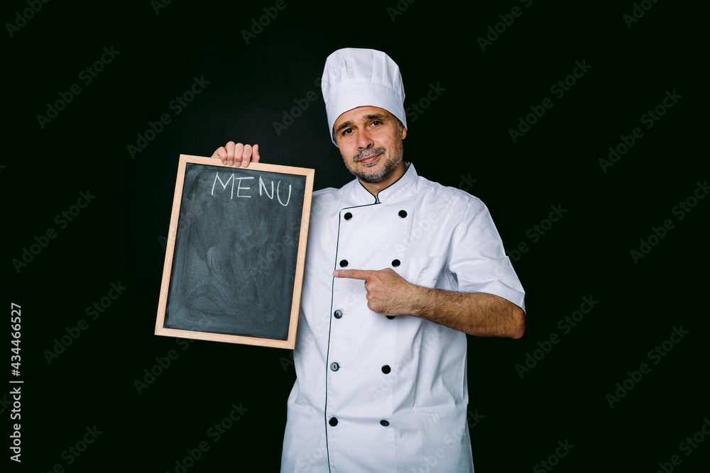 Chef cook in jacket and kitchen hat smiling, holding a piazarra with the menu, on black background Chef cook in jacket and kitchen hat smiling, holding a piazarra with the menu, on black background