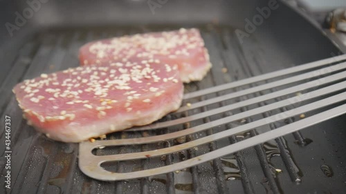 Flipping a steak of yellowfin tuna on a grilling pan in 4K. Concept turning on the other side and frying and cooking tuna steak in slow motion.