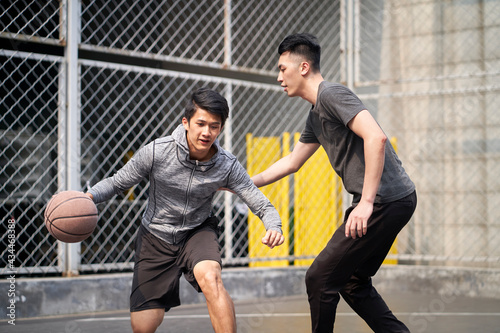 two young asian men playing one on one basketball on outdoor court