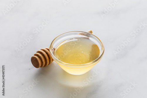 Close up a small glass bowl of honey with a honey wand in behind.