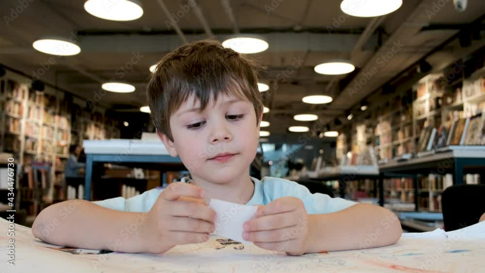 Engaged young boy with brown hair examines white paper piece