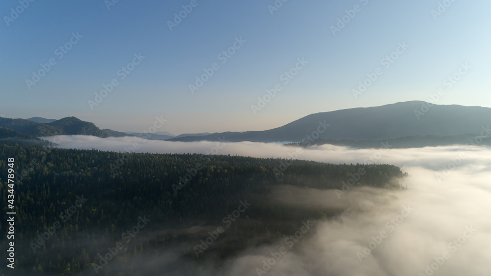 Aerial view: Mist or sea of fog cover the mountains valley. Cloudy view on top of a mount with clouds at foreground and background. ocean of clouds