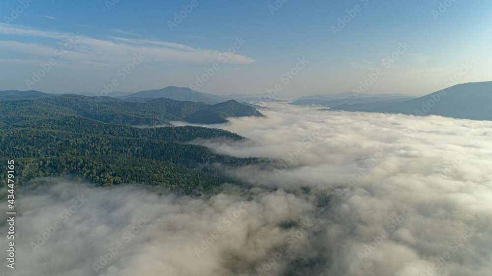 Aerial view: Mist or sea of fog cover the mountains valley. Cloudy view on top of a mount with clouds at foreground and background. ocean of clouds