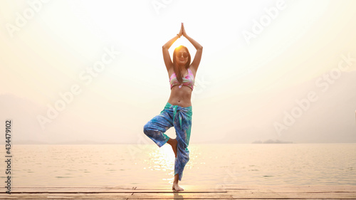 Yoga on the beach. Happy asian woman wearing Tie Dye bikini practicing yoga. Young healthy woman on Summer yoga at sunset seashore.