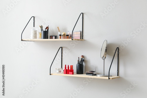 Modern shelves with decorative cosmetics and brushes hanging on light wall © Pixel-Shot