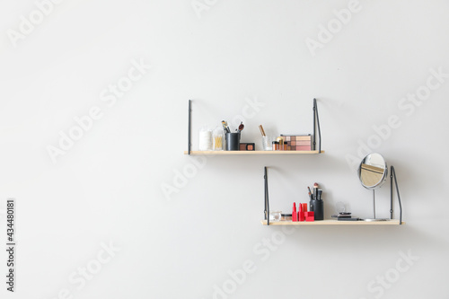 Modern shelves with decorative cosmetics and brushes hanging on light wall © Pixel-Shot
