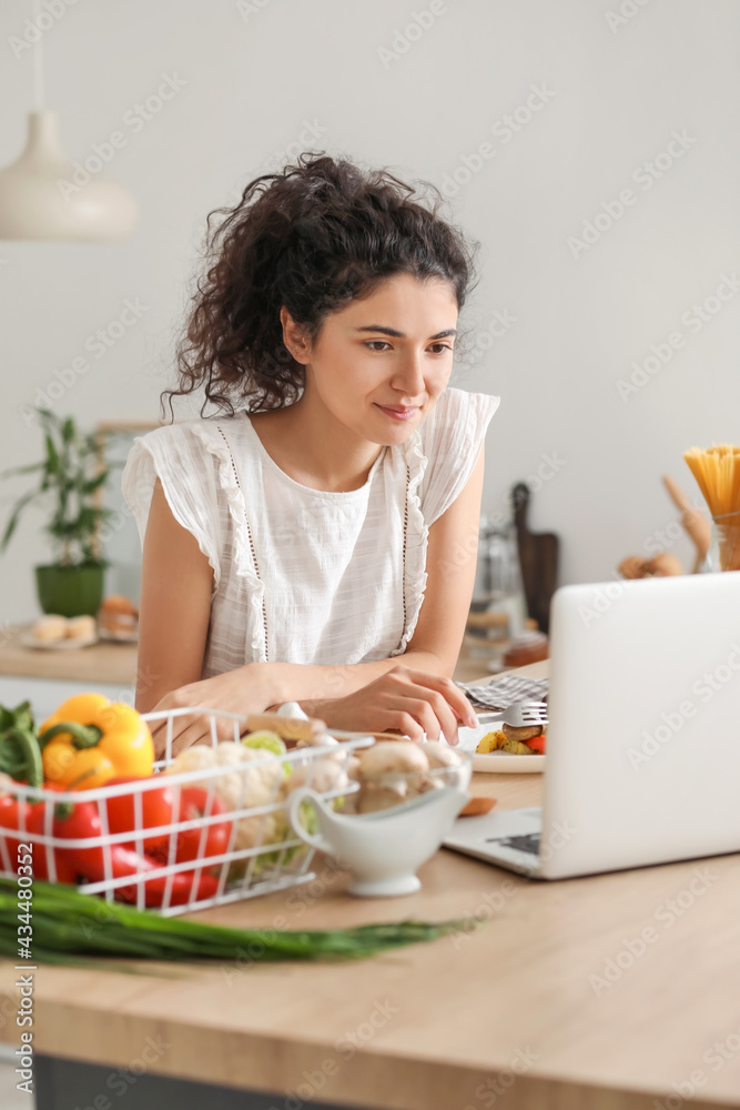 Young woman using laptop while eating in kitchen