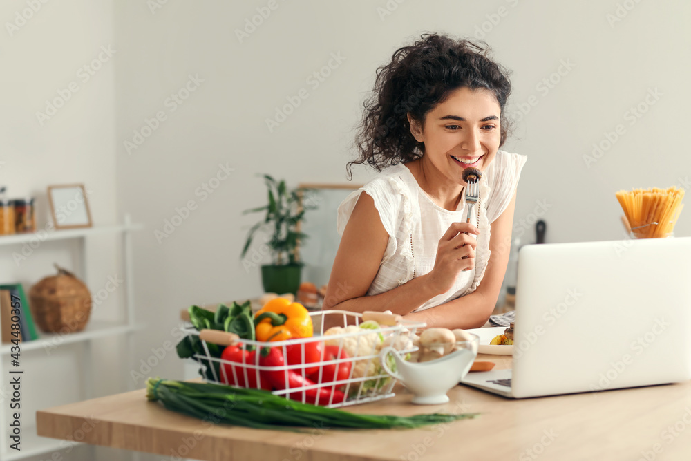 Young woman using laptop while eating in kitchen Young woman using laptop while eating in kitchen