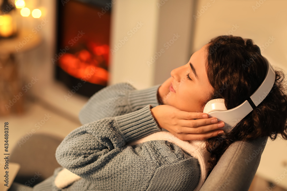 Fototapeta premium Beautiful woman with headphones near fireplace at home