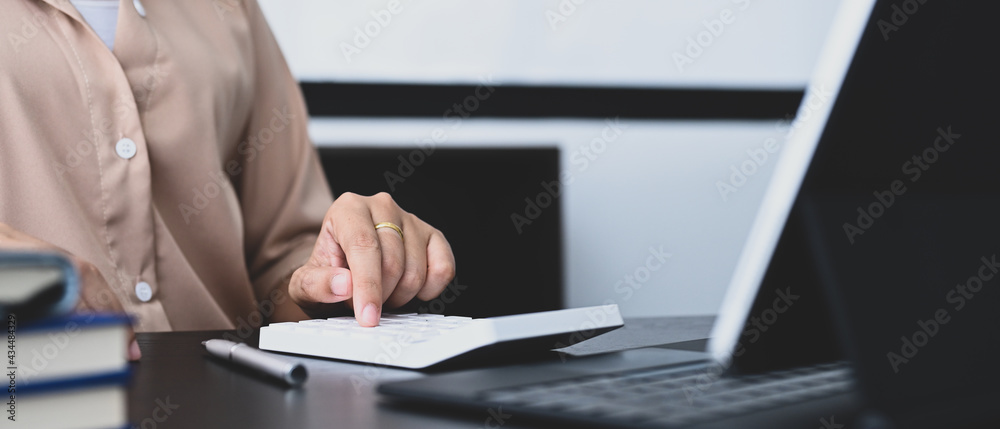 Cropped shot of female accountant using calculator and working with laptop at office desk. Cropped shot of female accountant using calculator and working with laptop at office desk.