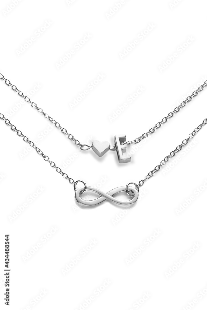 Cropped shot of two silver chains with charms shaped as infinity sign, heart and letter E. The piece of elegant jewelry is isolated on the white background. Cropped shot of two silver chains with charms shaped as infinity sign, heart and letter E. The piece of elegant jewelry is isolated on the white background.