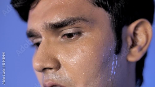 Portrait of youth with drops of sweat on his whole face - intense workout concept. Extreme closeup of an Indian male's face looking sideways while perspiring heavily - health activity concept